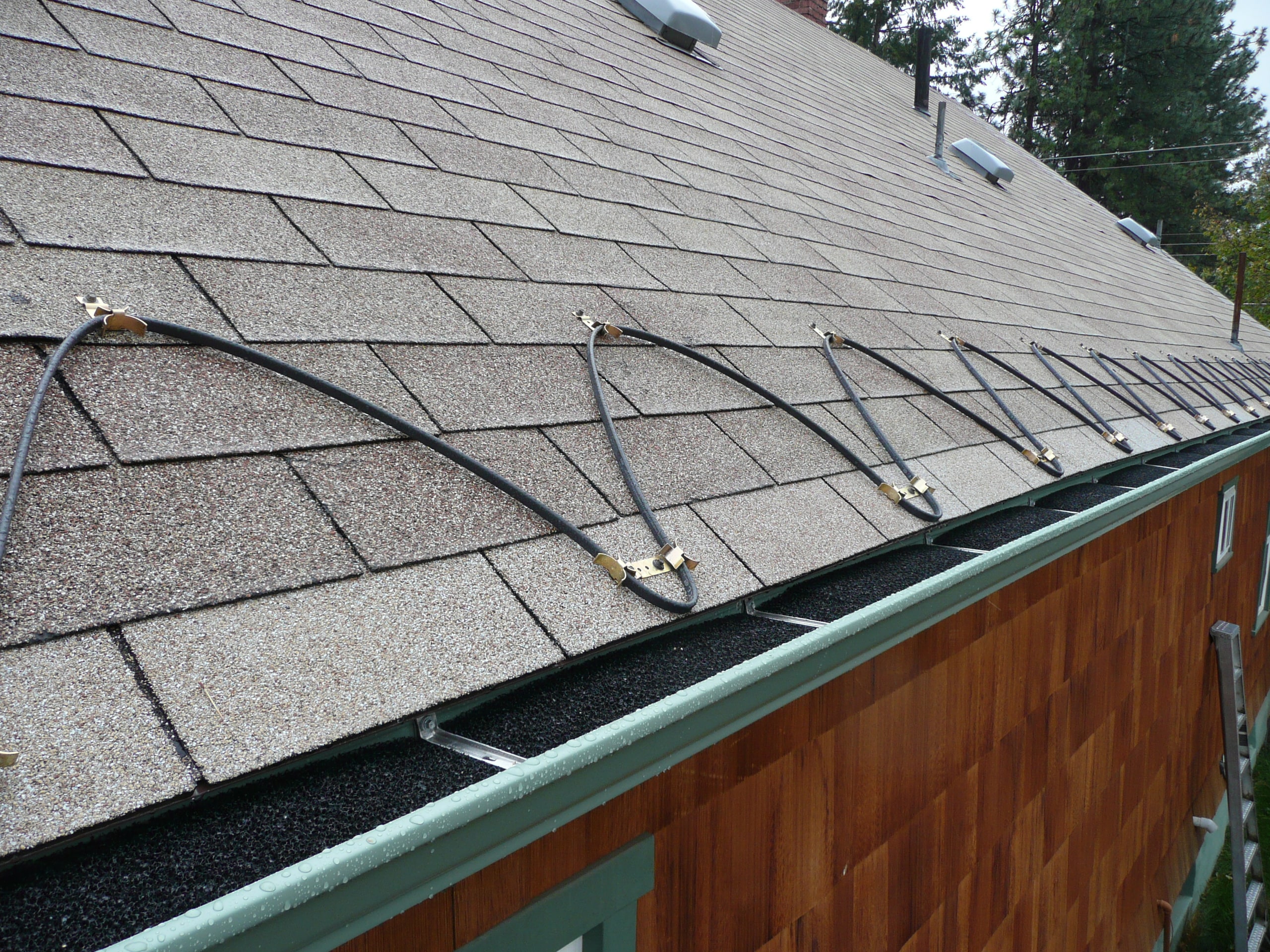 Heat trace cable run in loops along the eave of a shingle roof, above the gutter