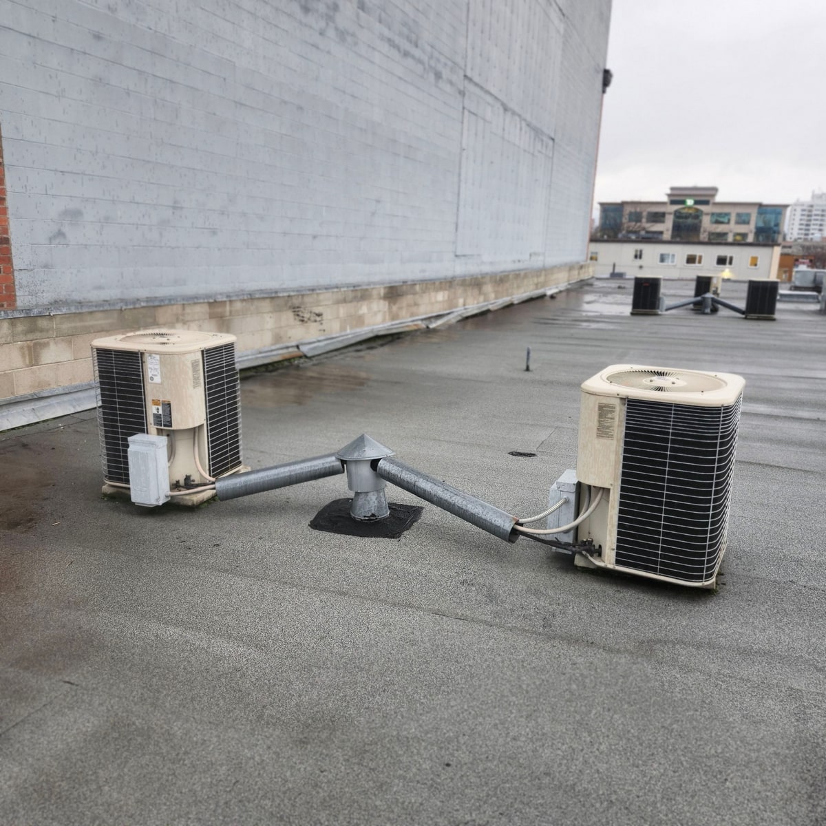 Two air-conditioning units on a pipe stand on the worn old roof