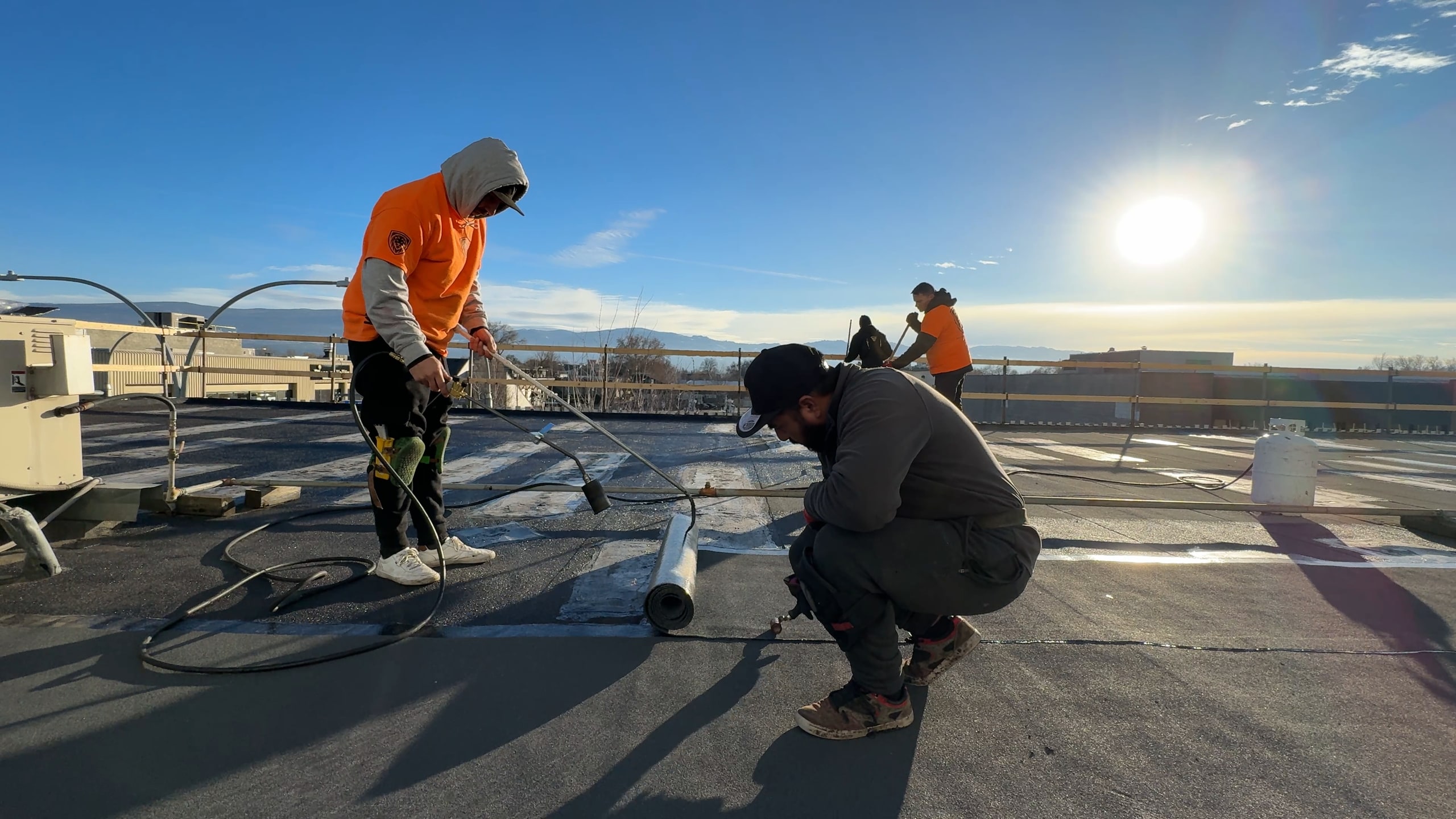 Roofers torching a new roof on over the old one, downtown, in low sun