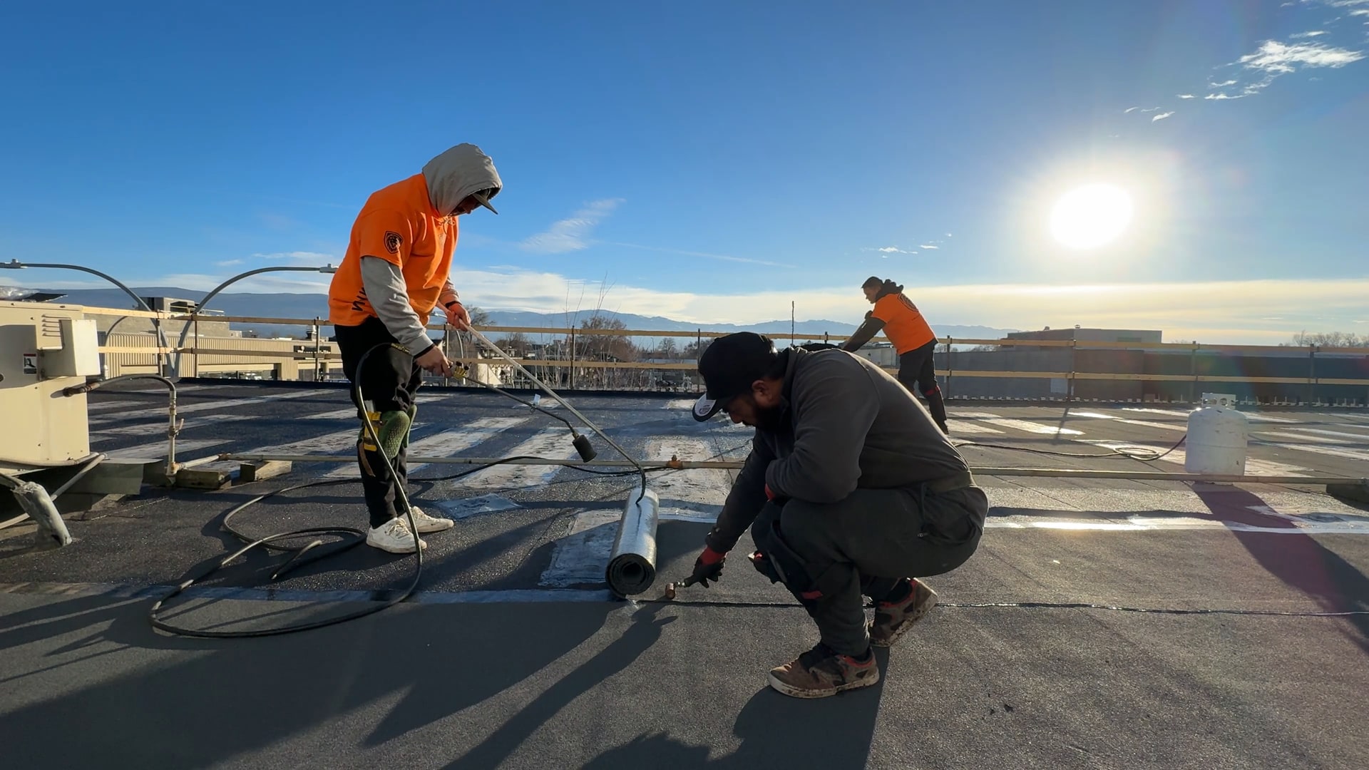 Roofers torching a new roof on over the old one, downtown, in low sun