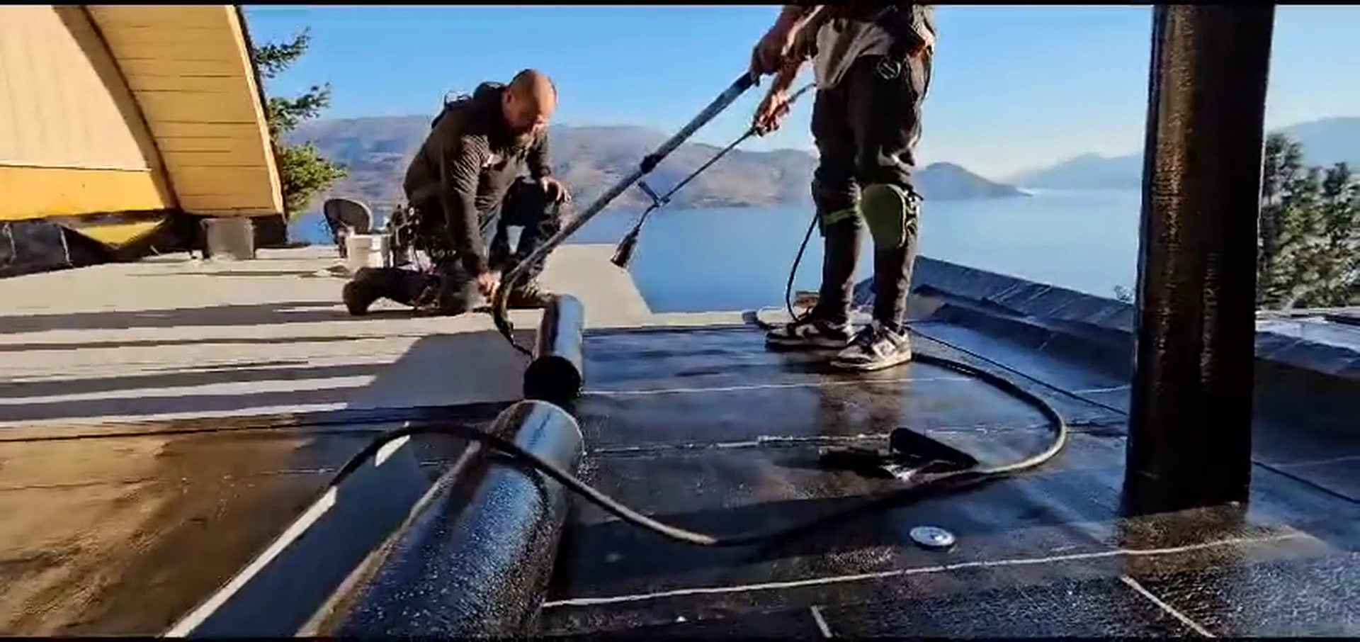Roofers torching a new flat roof down, Okanagan Lake behind